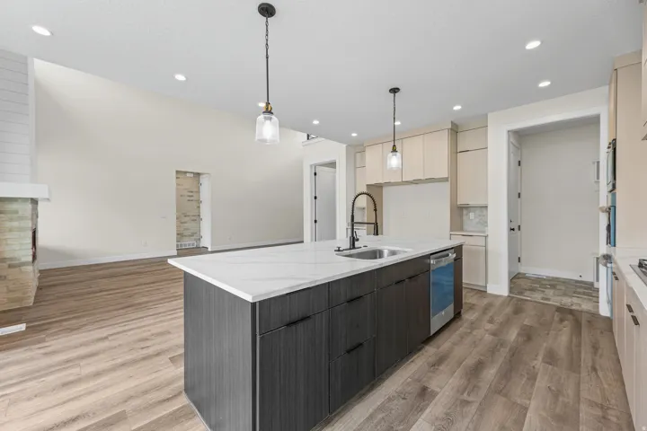 Kitchen island with a white countertop and integrated sink, stainless steel dishwasher, wood-finish flooring, recessed lighting, and pendant light fixtures