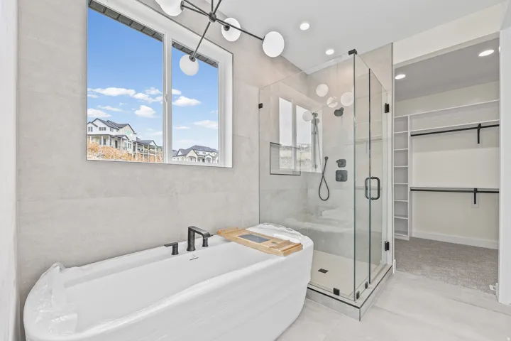 Freestanding soaking tub with dark-finish faucet, glass-enclosed shower with dark-finish fixtures, and a walk-in closet with built-in shelving