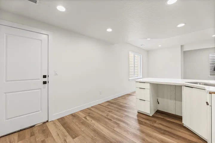 Modern primary closet featuring extensive white cabinetry with multiple drawers, a long countertop workspace, recessed ceiling lighting, and warm wood-finish flooring throughout