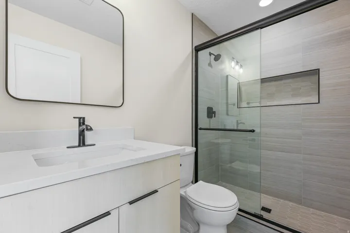 Vanity with integrated sink and matte black faucet, frameless mirror, walk-in shower with tiled walls, built-in shower niche, and glass enclosure