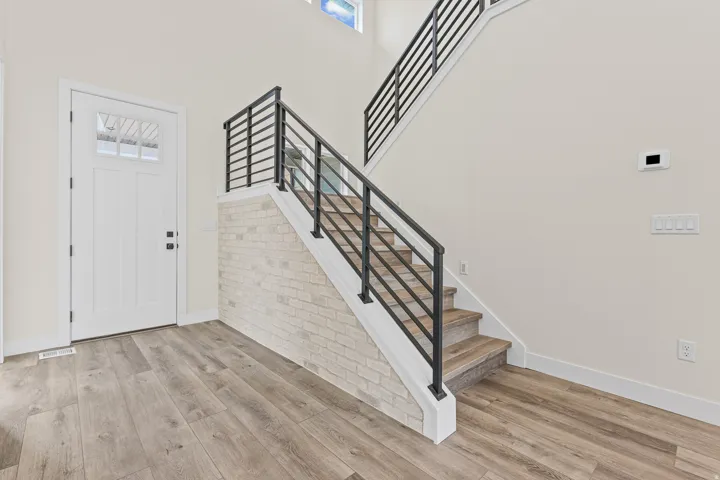 Wood-finish flooring, white paneled door with window inserts, and a staircase featuring a modern black metal railing