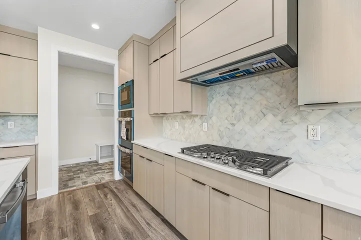 Contemporary kitchen featuring wood-finish flooring, light-toned cabinetry, white countertops, and a herringbone-patterned backsplash