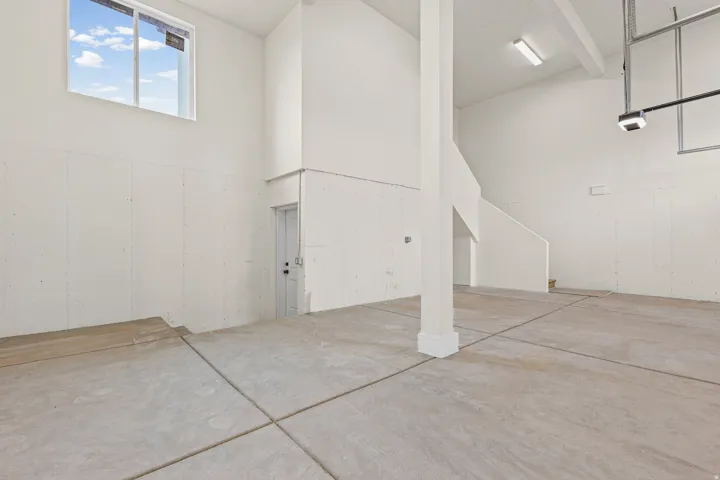Large open space with concrete flooring, high ceilings, a white-framed window, and a staircase
