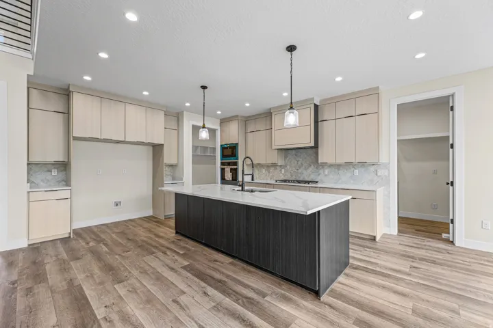 Contemporary kitchen featuring a large central island with a solid surface countertop, light wood-finish cabinetry, recessed lighting, and wood-finish flooring