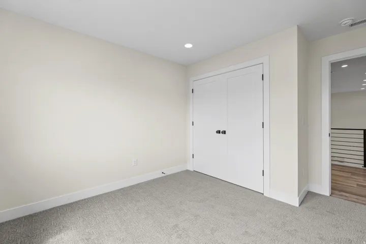 Neutral wall color, recessed lighting, white trim, light gray carpeting, and white bi-fold doors