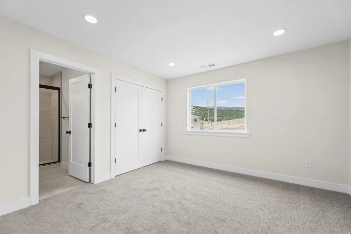 Recessed lighting, light-colored walls, window with outdoor scenery, carpeted flooring, and a bi-fold closet