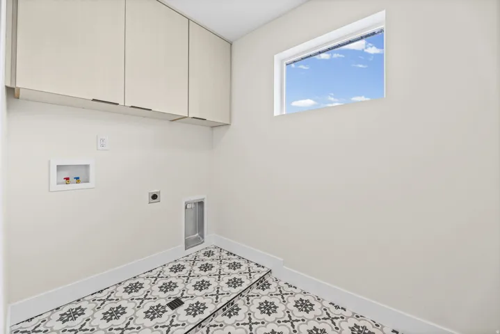 Patterned floor tile, overhead cabinetry, window, appliance hookups, and light-toned walls