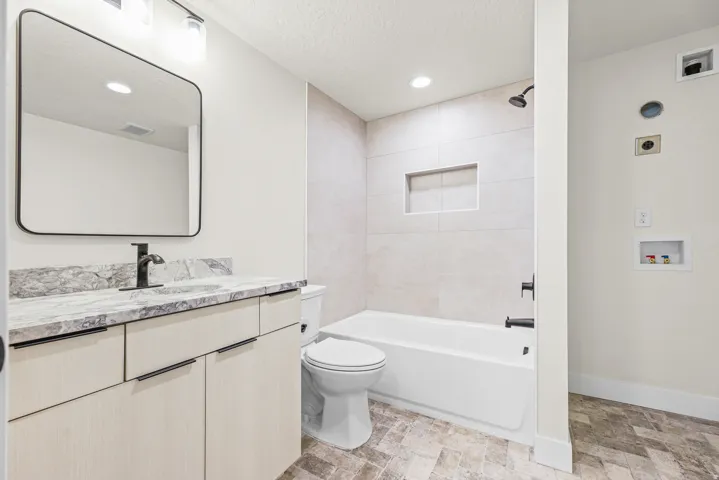 Vanity with integrated sink, rectangular mirror, light wood-finish cabinetry, and dark hardware