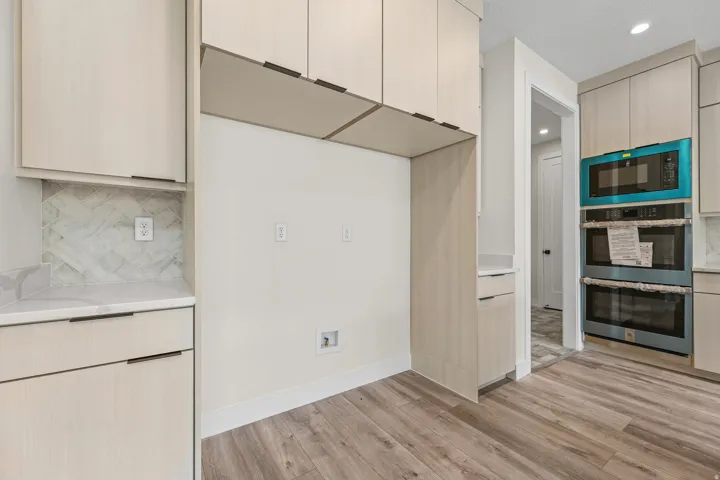 Light-toned cabinetry with recessed pulls, white countertops, herringbone tile backsplash, wood-finish flooring, and built-in double ovens
