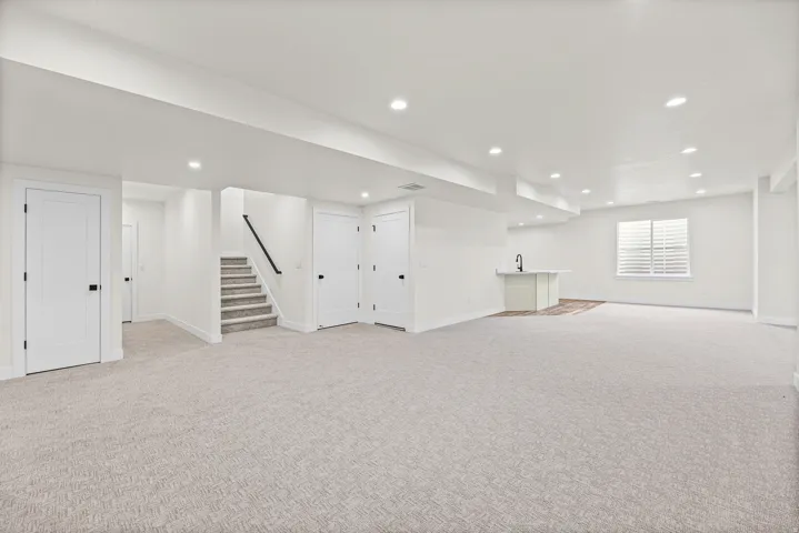 Expansive finished basement with recessed lighting, light-toned carpet, a built-in wet bar, and a window featuring white plantation shutters