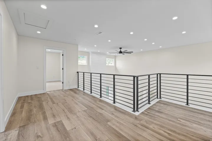 Spacious upper-level area with wood-finish flooring, recessed lighting, and a contemporary ceiling fan