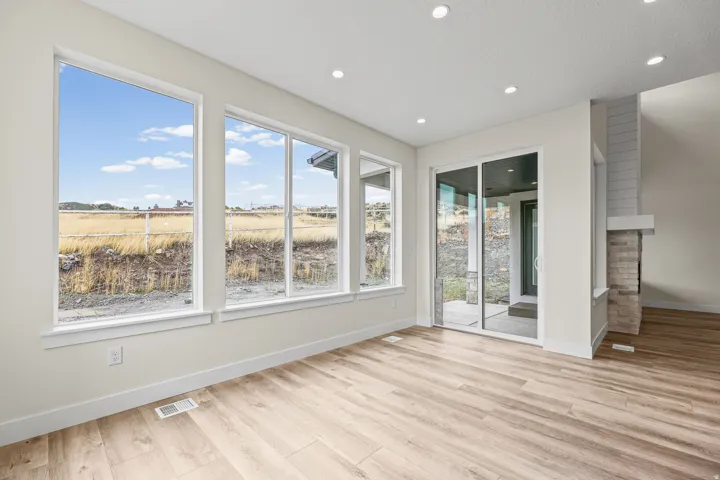 Wood-finish flooring, recessed ceiling lighting, multiple large windows, sliding glass door, and a stone-clad fireplace