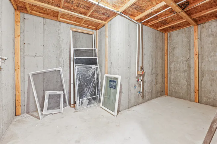 Unfinished basement with concrete walls and flooring, exposed wood ceiling joists, and visible utility lines