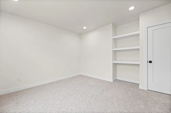 Recessed lighting illuminates the room, featuring built-in shelving, a neutral carpet, and white trim