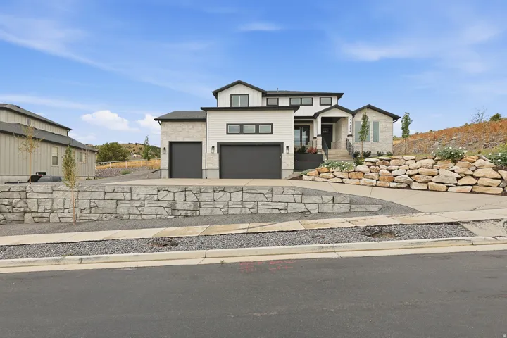 Contemporary exterior with mixed material facade, two-car garage, tiered retaining walls, concrete driveway, and mature landscaping
