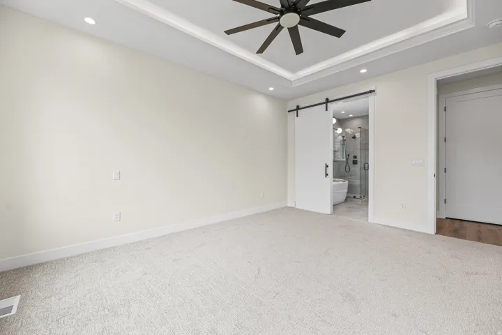 Tray ceiling with recessed lighting, ceiling fan, carpeted flooring, and a sliding barn door