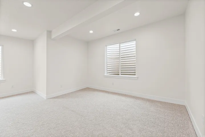 Recessed lighting, light-colored walls, patterned carpeting, white trim, and a window with a window well