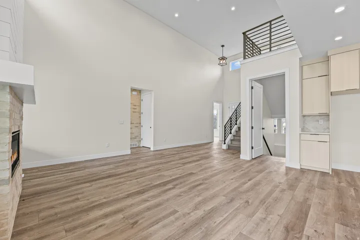 Vaulted ceilings with recessed lighting, wood-finish flooring, stone-clad fireplace with mantel, open-tread staircase with metal railing, and built-in cabinetry with stone backsplash