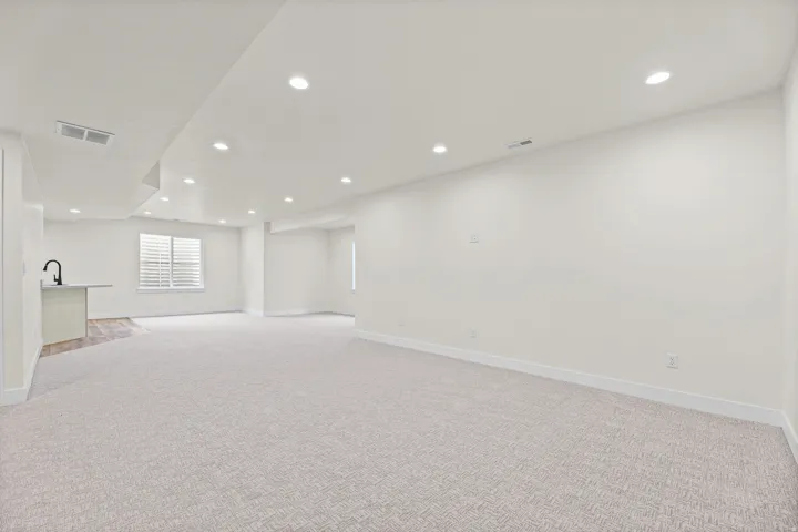 Spacious room featuring neutral carpeting, recessed lighting, a built-in wet bar with a black faucet, and a window with plantation shutters