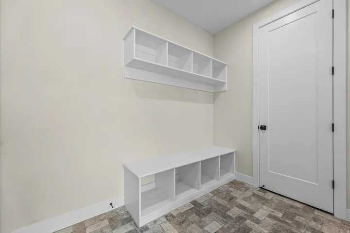 Built-in storage shelves and bench with cubbies, complemented by a white paneled door with black hardware, and patterned floor tiling