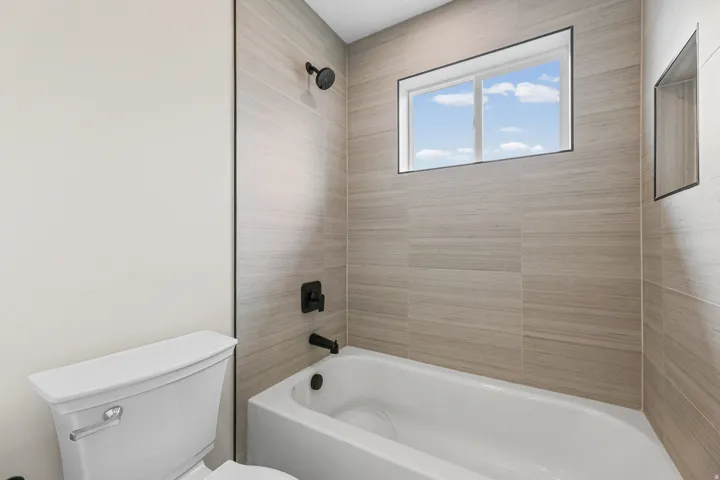 White tub and shower with matte black fixtures, surrounded by large format striped wall tile