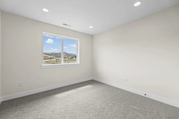 Recessed ceiling lighting, a large picture window, light-toned walls, and patterned carpeting