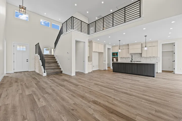 Vaulted ceilings, wood-finish flooring, two-story open concept, modern kitchen island, and contemporary black railing