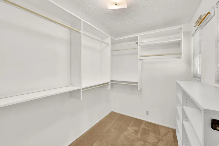 Spacious walk-in closet with extensive built-in shelving, multiple hanging rods, natural light from a window, and recessed ceiling lighting