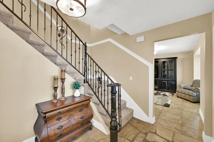 Staircase with wrought iron railing, carpeted treads, and flagstone-style tile flooring