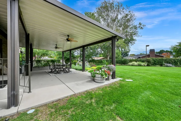 Covered concrete patio with multiple ceiling fans, featuring a metal railing and expansive green lawn