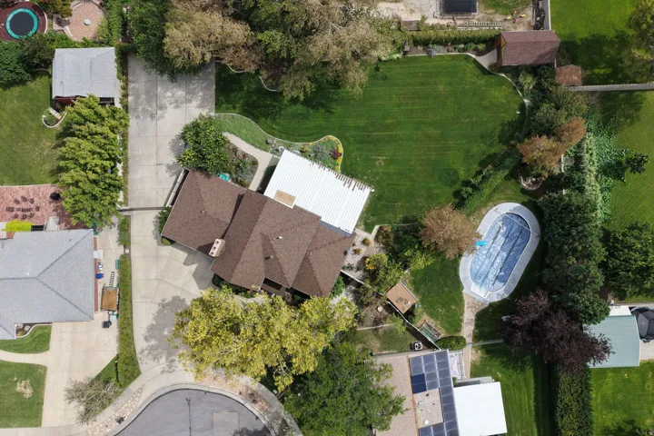 Expansive property featuring a brown shingled roof, a covered swimming pool, a large manicured lawn, and mature trees