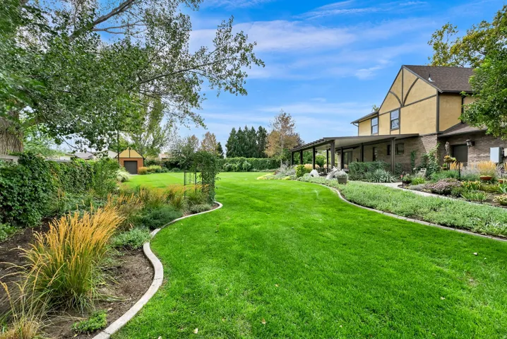 Expansive lawn with established landscaping, a Tudor-style exterior, and an extended covered patio