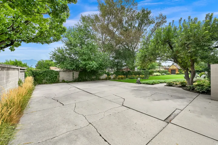 Expansive concrete pad, lush lawn, mature trees, and a decorative block wall