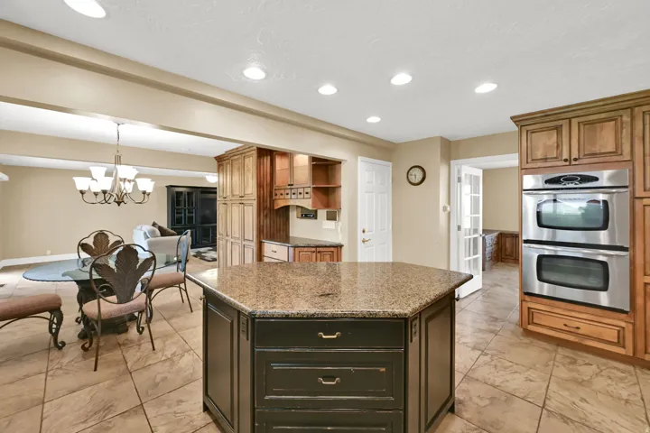 Kitchen featuring a hexagonal island with a stone countertop, built-in double ovens, and tile flooring