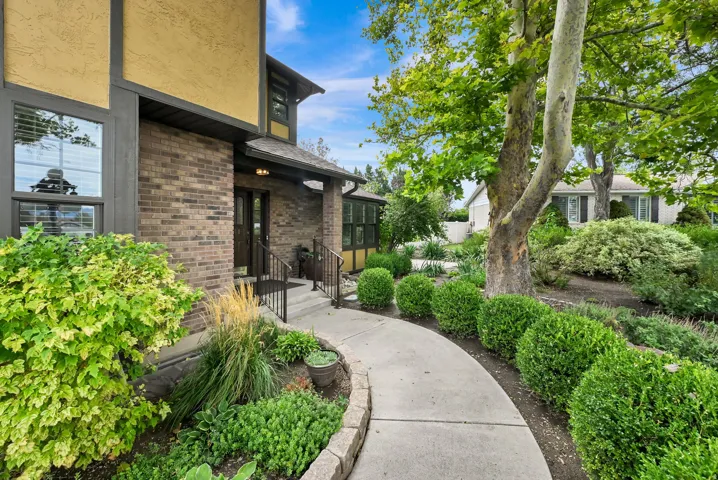 Brick facade with painted stucco accents, concrete walkway, wrought iron handrails, and mature landscaping