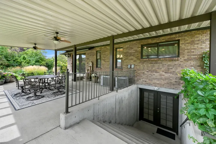Expansive covered patio with concrete flooring, dual ceiling fans, and a metal railing system