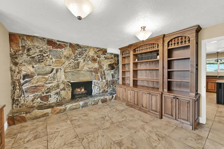 Stone-clad fireplace, integrated wooden shelving, built-in cabinetry, and tile flooring