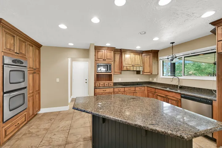 Spacious kitchen featuring a central island with granite countertops, abundant wood cabinetry, stainless steel double wall ovens, a built-in microwave, and recessed lighting