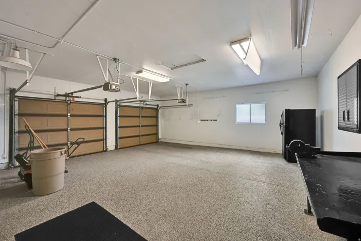 Two garage doors with automatic openers, concrete flooring with an epoxy finish, a single window, and overhead fluorescent lighting
