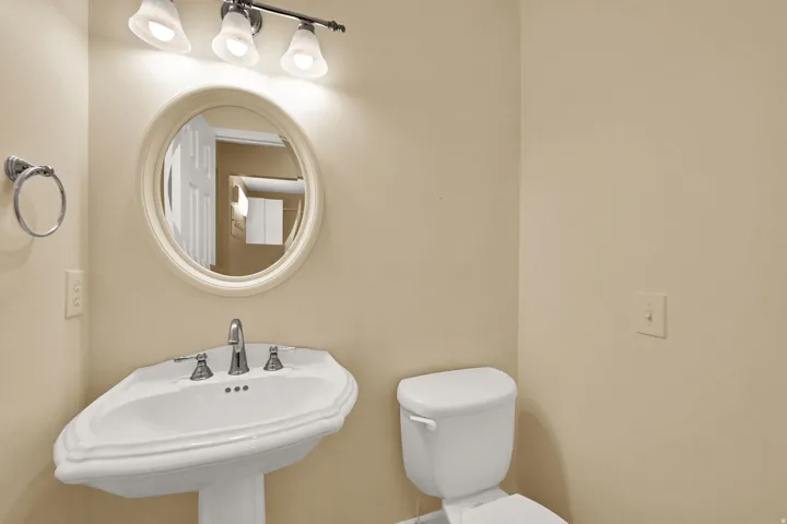 Pedestal sink, round framed mirror, three-light vanity fixture, chrome faucet, and white toilet