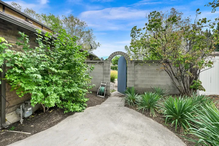 Arched garden gate set into a block wall, paved pathway, established perimeter landscaping, and brick exterior