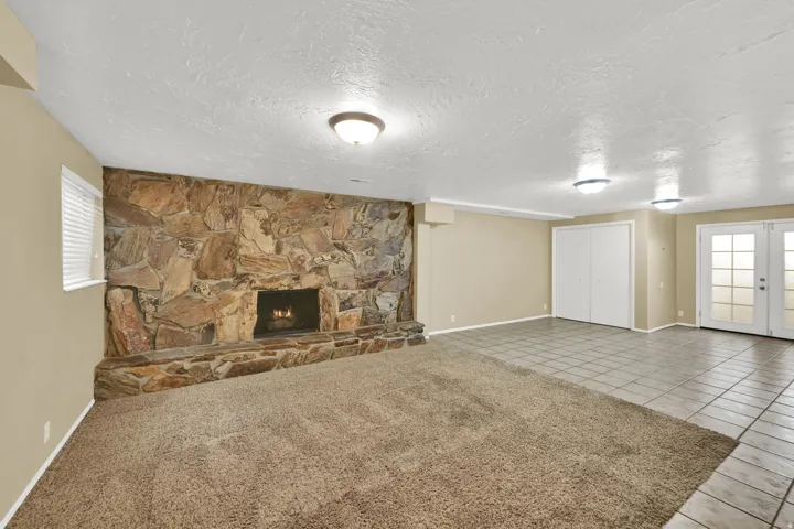 Stone accent wall with a fireplace, carpeted flooring, tiled flooring, built-in closet with bi-fold doors, and French doors with privacy glass