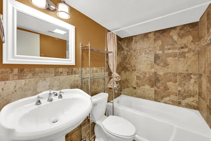 Pedestal sink with chrome fixtures, full bathtub, and extensive tile surround
