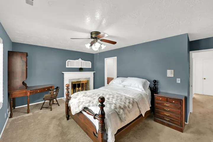 Carpeted room featuring a white fireplace with a decorative mantel and a ceiling fan with light fixture