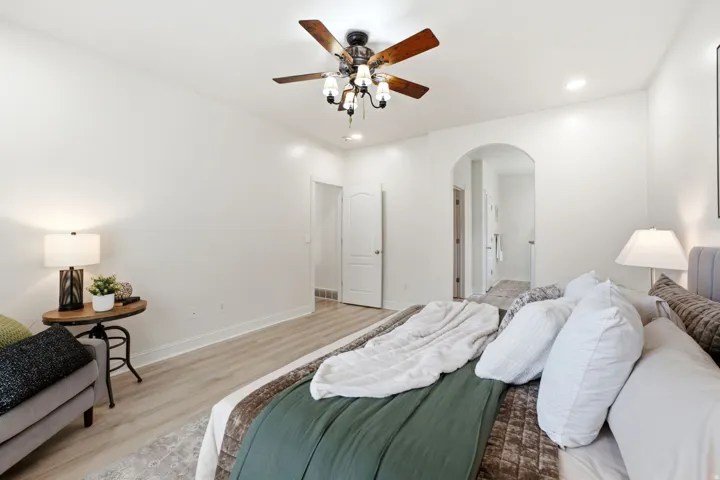 Recessed lighting, wood-finish flooring, ceiling fan with integrated lighting, and an arched doorway going into a luxurious bath and huge closet