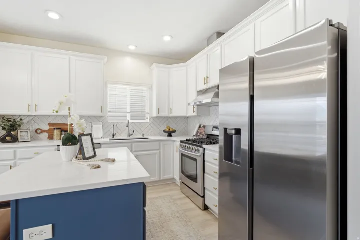 Kitchen featuring white cabinetry, a blue-finished island with a light-toned countertop, stainless steel appliances, and wood-finish flooring