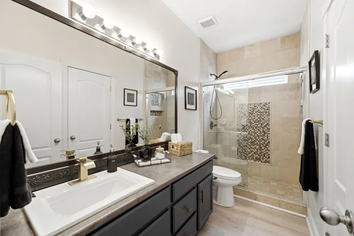 Bathroom featuring a single vanity with dark cabinetry, integrated sink, and gold-finish faucet