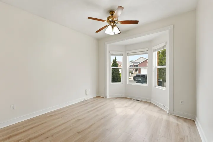 Bay window with multiple panels, wood-finish flooring, ceiling fan with integrated lighting, and neutral wall tones