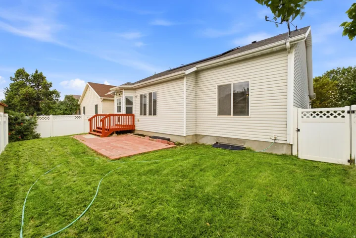 Expansive green lawn, red-toned wood deck, brick paver patio, white lattice fencing, and light-toned siding