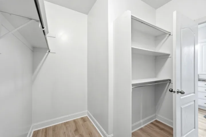 Walk-in closet with shelving, hanging rods, and wood-finish flooring